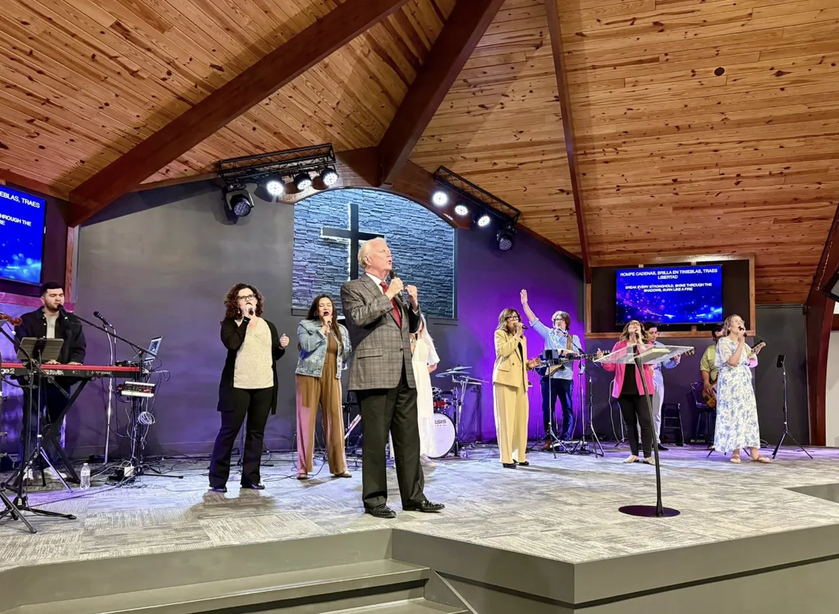 The worship team singing under a wood ceiling while the screen shows the lyrics in Spanish and English