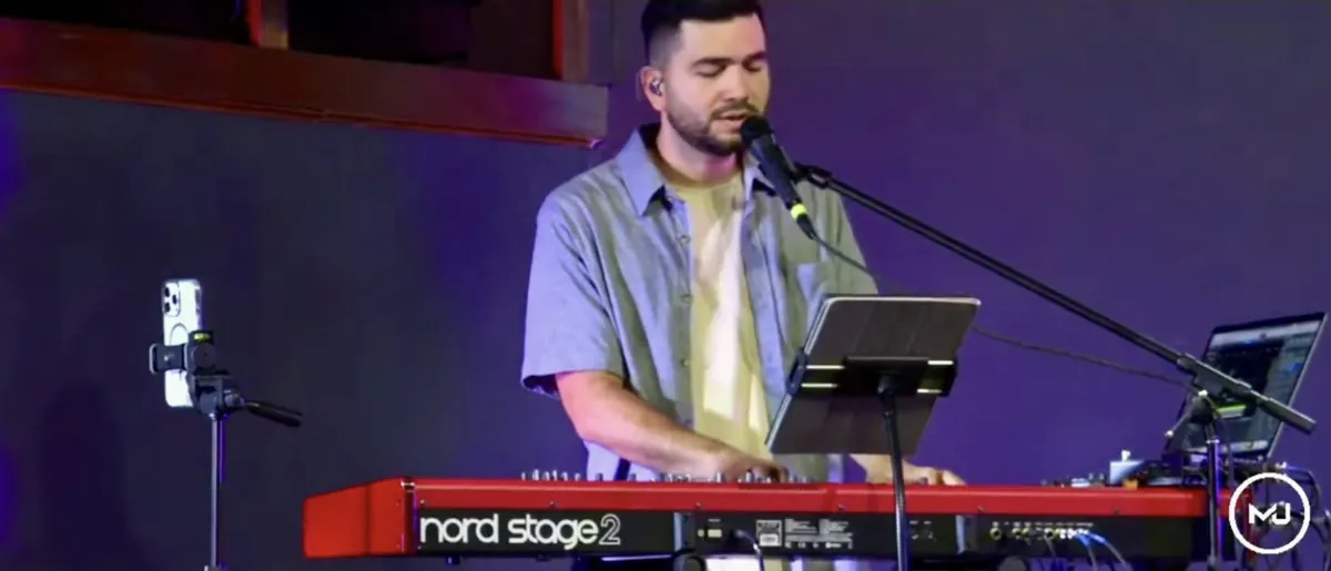 A young man singing at the keyboard under violet stage light.