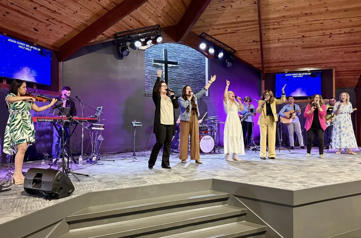 Singers with hands raised in worship, a violinist and the band on the stage at Mt. Juliet Church of God