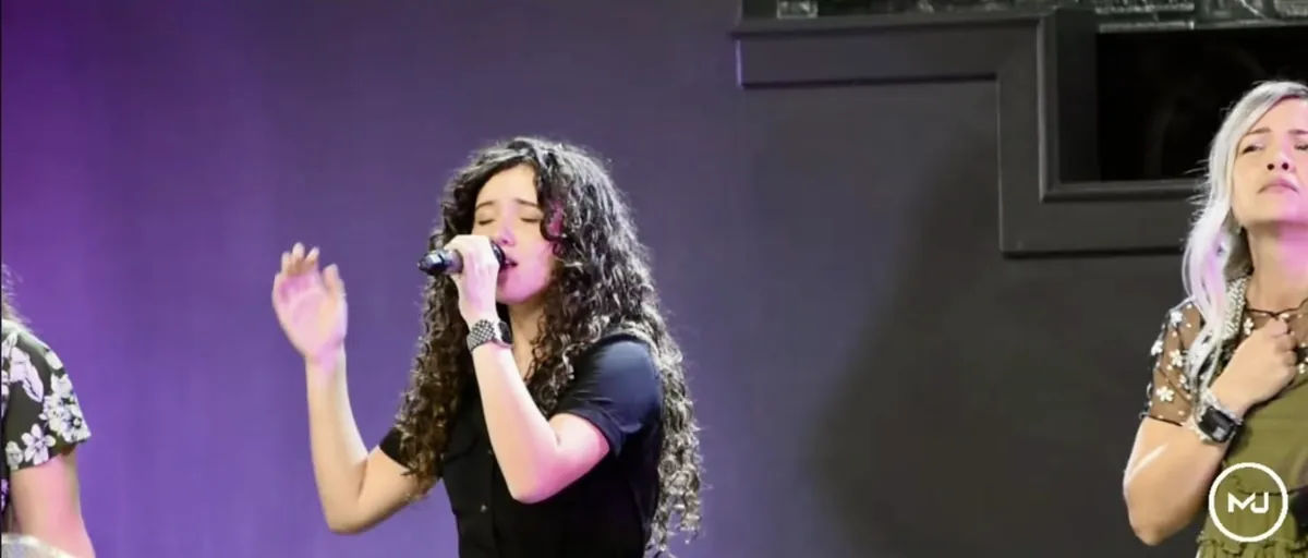 A worship leader singing with her eyes closed and her hand lifted.