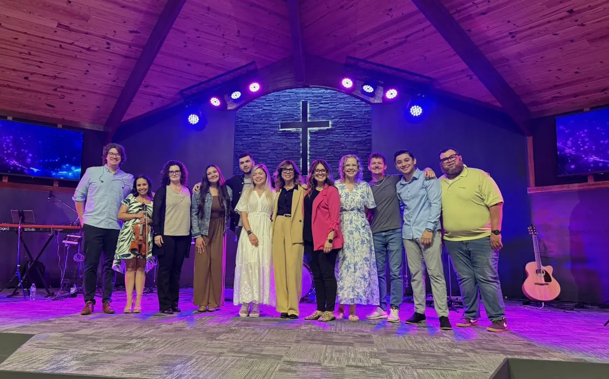 The worship team and staff smiling together on stage in front of the cross