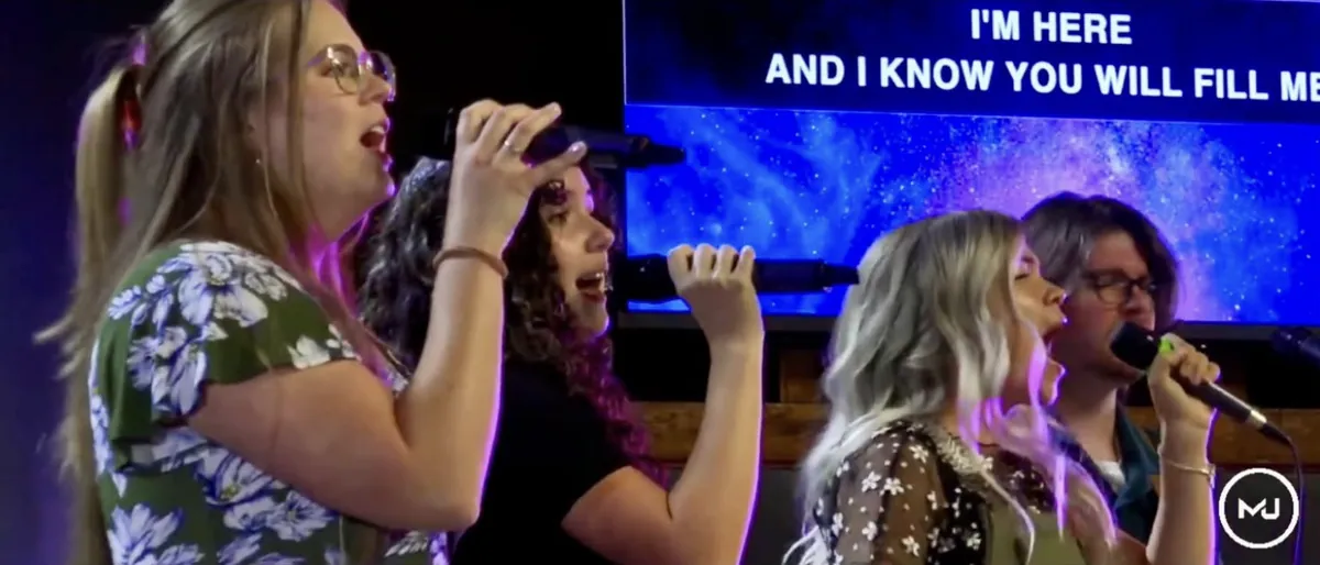 Singers worshipping together with song lyrics on the screen behind them