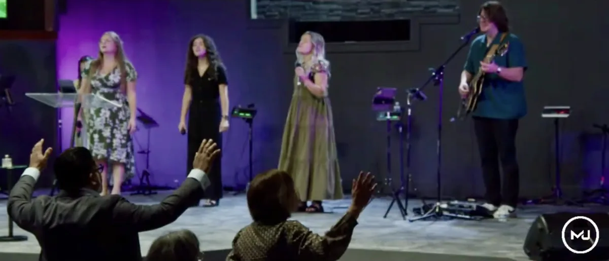 Worshippers lifting their hands toward the singers on a violet-lit stage